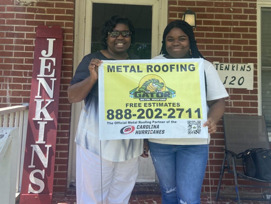 Two homeowners holding a sign: Call us today to schedule your free estimate on new roofing in NC and SC, (888) 202-2711.