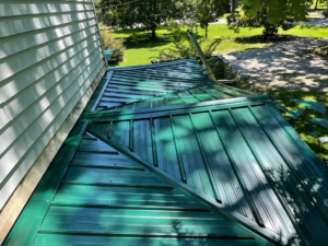 A portion of a metal roof painted green with shadows from nearby tree branches.
