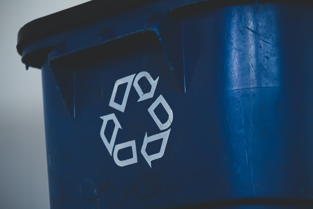 A blue colored dust bin with a recycling symbol over it.