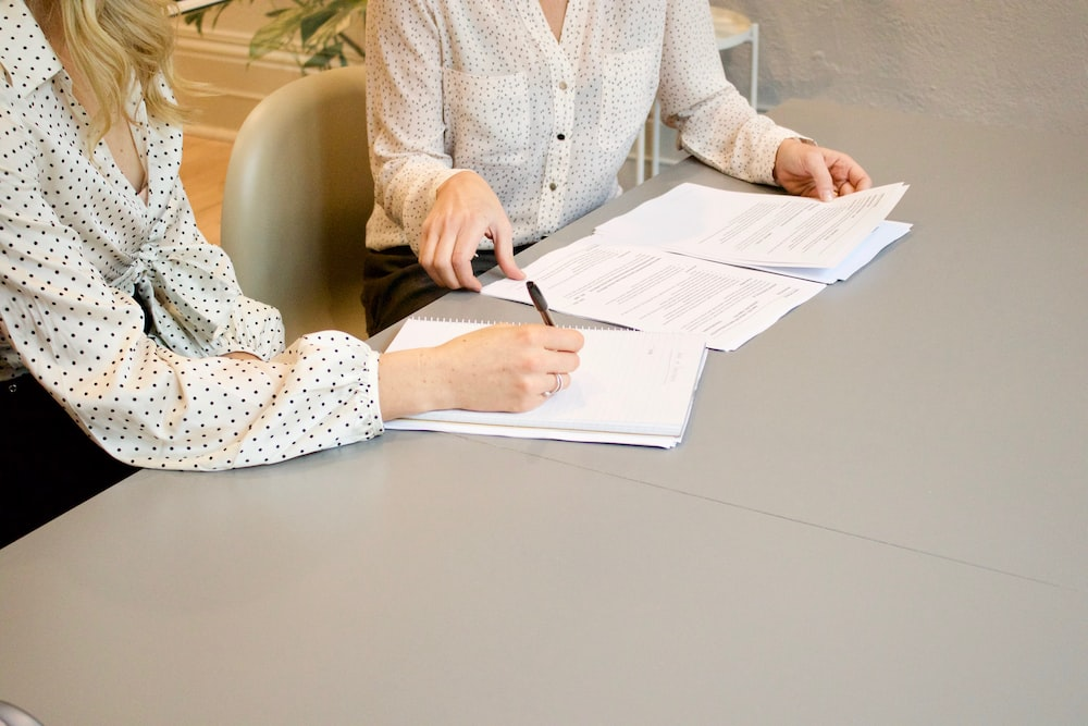 two people signing different kinds of documents over a table.